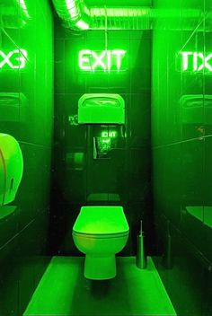 a green toilet in a bathroom with exit signs on the walls and lights above it