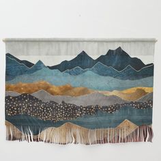 a tapestry hanging on a wall with mountains in the background and fringes around it