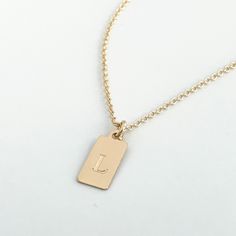 This mini dog tag necklace is perfect for every day wear. This engraved necklace features a small dog tag shaped rectangle in 14k gold fill or sterling silver engraved with a letter of your choice. The font comes in your choice of the classic style (in the photo) or script as shown on the photos. Your new letter or initial necklace will arrive in a complimentary gift box. Please be sure to indicate if you want the script font, otherwise your necklace will be engraved with the classic style. Othe Personalized Gold Dog Tag Charm Necklace, Personalized Gold Rectangular Charm Necklace, Simple Engraved Gold Charm Necklace, Simple Gold Engraved Charm Necklace, Gold Hand Stamped Dog Tag Jewelry, Hand Stamped Gold Dog Tag Jewelry, Minimalist Personalized Dog Tag Jewelry, Rectangular Tag Jewelry For Gifts, Gold Rectangular Charm Necklace For Personalized Gift