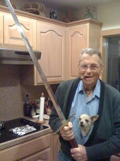 an old man holding a large knife with a dog on it's chest in his lap