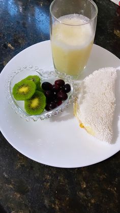 a white plate topped with a slice of cake next to a bowl of fruit and a glass of juice