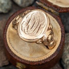 a gold monogrammed ring sitting on top of a wooden box next to rocks