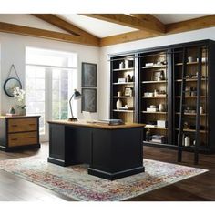 an office area with desk, bookcases and large rug in front of windows