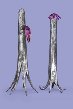 two tall metal sculptures with pink flowers in them on a purple background, one is standing up and the other is sitting down