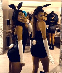 two women dressed up in bunny ears taking pictures with their cell phones while standing next to each other