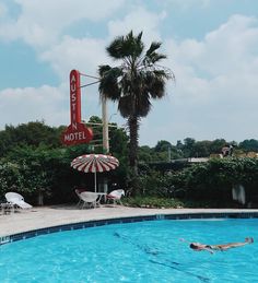 a motel sign next to a swimming pool with chairs and umbrellas in the foreground