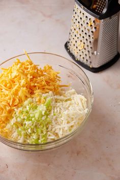 a glass bowl filled with shredded cheese next to a grater on top of a counter