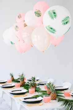 a table topped with lots of balloons and pineapples on top of white plates