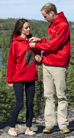 a man and woman standing on top of a mountain looking at something in their hands