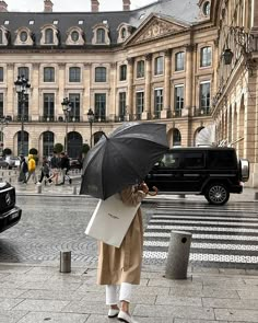 a woman holding an umbrella in front of a large building with cars parked on the street