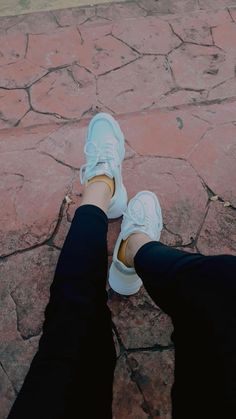 a person wearing white tennis shoes standing on a brick walkway with their legs crossed and one foot in the air