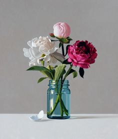 three different colored flowers in a blue glass vase on a white table top with one pink and one red flower