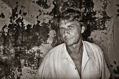 black and white photograph of a man in front of a wall with peeling paint on it