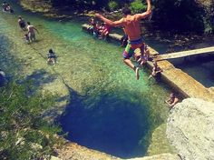 a man is jumping into the water from a cliff near some people in bathing suits