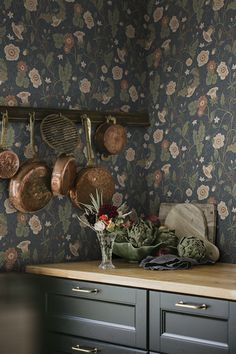 pots and pans are hanging on the wall next to a kitchen counter with flowers