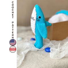 a crocheted blue and white toy shark next to a box