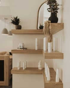 three wooden shelves with plants and candles on them in a room that has white walls