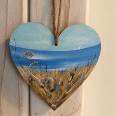 a painted heart hanging on the side of a door with sea grass and birds in it