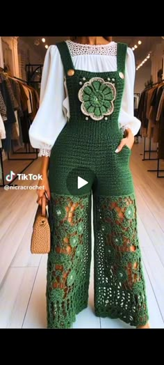 a woman wearing green crochet overalls and holding a purse in her hand