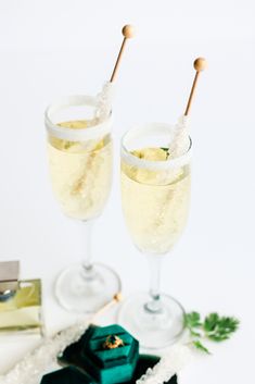 two wine glasses with champagne and green bow on white tablecloth next to small gift box