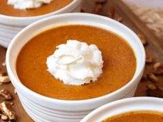 three white bowls filled with carrot soup and topped with whipped cream on a wooden board