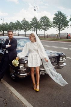 a man and woman standing next to a black car