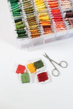 the scissors are next to many different colored thread spools and needles in a plastic container