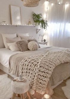 a white bedroom with lots of pillows and blankets on the bed, lights in the corner