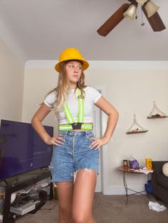 a woman in overalls and a yellow hat standing next to a tv with her hands on her hips