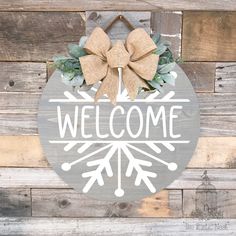 a welcome sign hanging on the side of a wooden wall with a bow around it