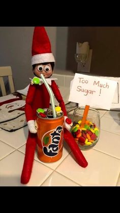 an elf is sitting on the kitchen counter next to a jar of candy and a sign that says too much sugar 1