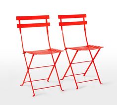 two red folding chairs sitting side by side on a white surface with one chair facing the other