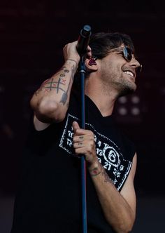 a man with tattoos on his arm holding a microphone and smiling at the camera while standing in front of an audience