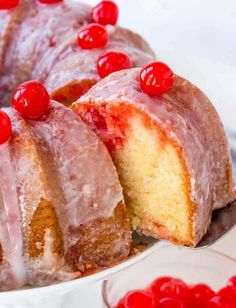 a bundt cake with pink icing and cherries on top is cut into slices