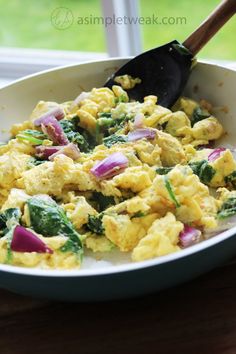 scrambled eggs with spinach and onions in a white bowl on a wooden table next to a window