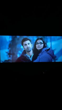 a man and woman standing in front of a tv screen with the same image on it