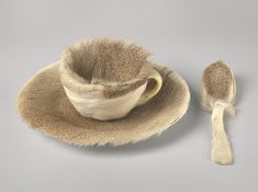 a cup and saucer on a plate with a tassel around the edge, sitting on a gray surface