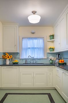 a kitchen with white cabinets and blue counter tops, sunflowers on the window sill