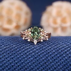 a ring with an oval green stone surrounded by leaves on top of a blue blanket