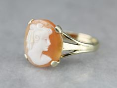 Crafted with a simple, classical style, this solitaire ring will be the perfect accessory for any occasion! This round Cameo has wonderful crisp details and a great contrast between the carving and the peach background. Cameo is the art of carving a layered material, creating a portrait or landscape in the differing colors and textures.  Metal: 10K Yellow Gold Gem: Cameo Gem Measurements: 13.2 mm, Round Ring Size: 6.50 Marks: "10K" Stamped on the inside band Yellow Gold Sapphire Ring, Peach Background, Retro Era, Classical Style, Cameo Ring, Vintage Cameo, Round Rings, July Birthstone, Hand Engraving