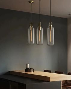 three glass pendants hang from the ceiling above a dining room table with brown chairs