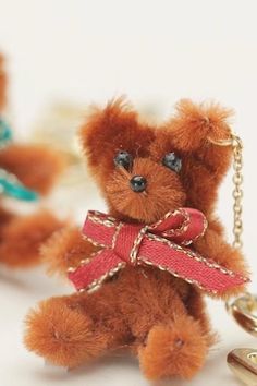 a brown teddy bear with a red ribbon on it's neck sitting next to two key chains