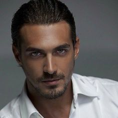 a close up of a person wearing a white shirt and looking at the camera with a serious look on his face