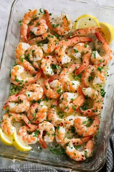 a glass dish filled with shrimp and garnished with parsley, lemon wedges