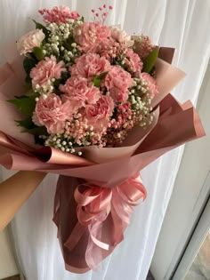 a bouquet of pink carnations and baby's breath tied to a ribbon