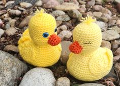 two crocheted yellow ducks sitting next to each other on top of some rocks