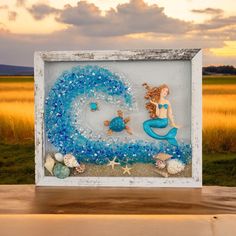 a glass frame with a mermaid and sea shells in it