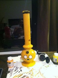 a yellow candle holder sitting on top of a table next to paint and other items