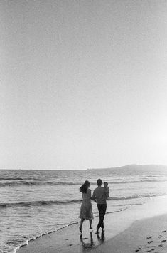 two people are walking along the beach near the water