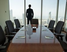 a man standing at the end of a conference room table in front of large windows